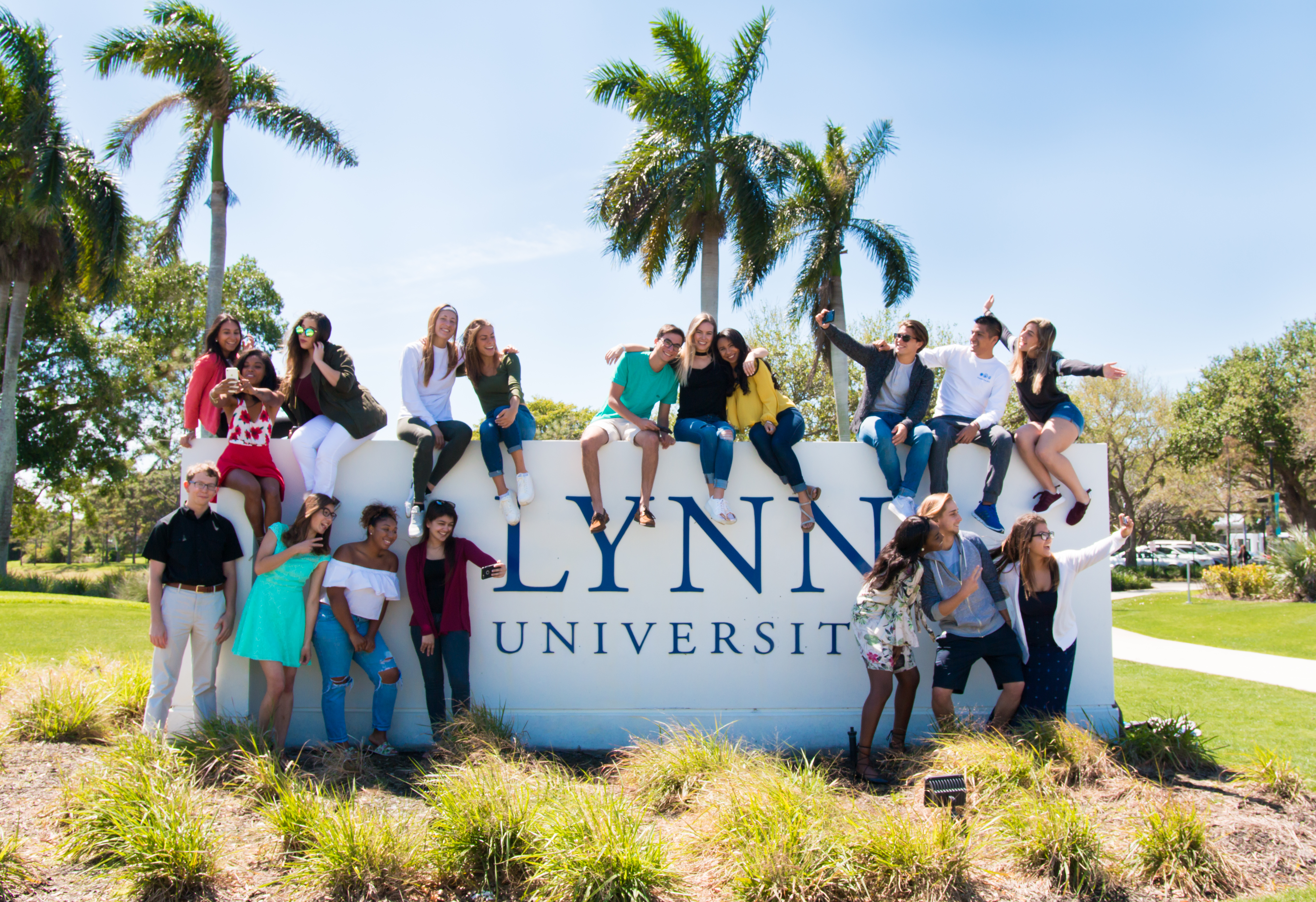 Students sitting on and in front of the Lynn University wall at the main entrance to campus